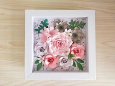 paper flowers in a white frame on a wooden table