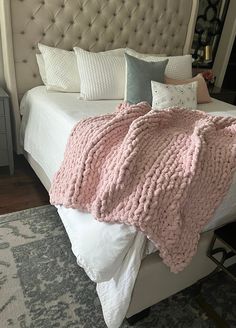 a bed with a pink blanket on top of it next to a night stand and nightstand