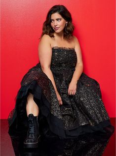 a woman in a black dress is sitting on a red background