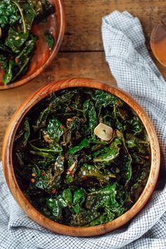 a wooden bowl filled with spinach next to a glass of beer on top of a table