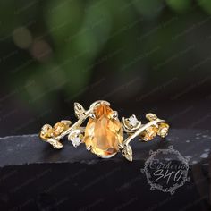 a ring with an orange stone surrounded by gold leaves on a black piece of wood