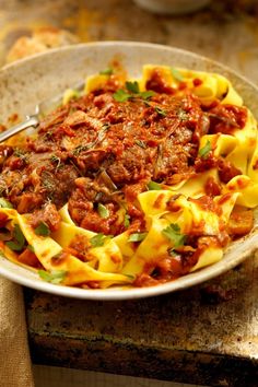 a white bowl filled with pasta covered in meat and sauce on top of a wooden table