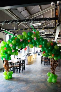 green balloons are hanging from the ceiling in an open space with tables and chairs around them