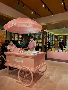 a pink ice cream cart with an umbrella on display in a store filled with people