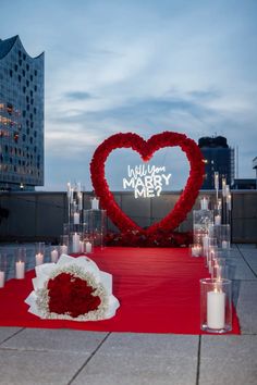 a heart - shaped sign is surrounded by candles and flowers at the end of a red carpet