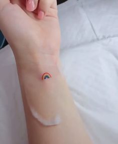 a woman's arm with a small rainbow tattoo on the left side of her wrist