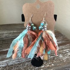 the earrings are decorated with feathers, beads and metal hooks on a wooden table next to a card board