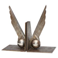 a pair of metal bookends with wings on each one and a ball in the middle