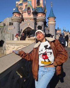 a woman standing in front of a castle wearing a mickey mouse t - shirt and jacket