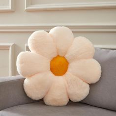 a white flower shaped pillow sitting on top of a gray couch next to a wall