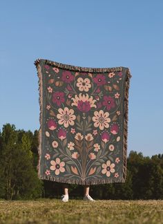 a woman is standing in the grass with a blanket on her back that has flowers and leaves