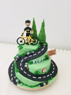 a birthday cake with a man riding a bike on top of the road and trees