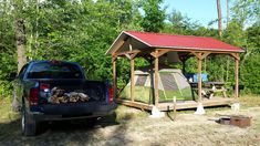 a truck is parked in front of a tent and firewood pile on the ground