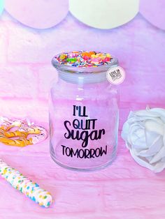 a jar filled with sugar and sprinkles on top of a pink table