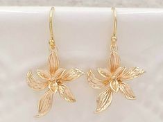 "These are pair of sophisticated and lovely orchid earrings. The beautiful shinning golden plated flower are enhanced with brushed stroke petals. They hang underneath golden plated French ear wires. The earrings measure approximately (32mm) 1.3 inches from the top of the ear wires to the bottom of the flowers. They are perfect for many occasion and everyday wear. They are also a great idea for gift giving and as a little treat for yourself. Your earrings will present in a gift box and tied with Cheap Gold Earrings With Birth Flower Detail, Gold Flower-shaped Earrings For Anniversary, Gold Earrings With Flower Charm In Delicate Style, Gold Flower-shaped Anniversary Earrings, Gold Dangle Flower Earrings For Bridesmaids, Party Jewelry With Gold Flower Decoration, Gold Jewelry With Flower Decoration For Parties, Delicate Gold Flower Charm Earrings, Delicate Gold Flower Earrings With Charm