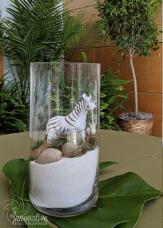 a glass vase filled with rocks and a small toy zebra on top of the base