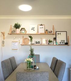 a dining room table with chairs and shelves on the wall above it that have flowers in vases