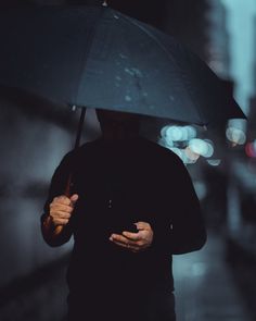 a man walking down the street holding an umbrella over his head while looking at his cell phone