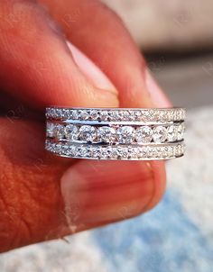 a hand holding a ring with three rows of diamonds on it's sides,