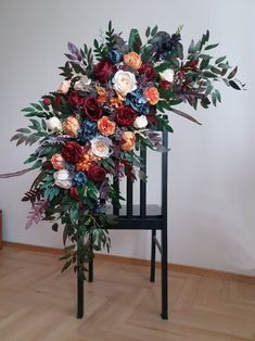 an arrangement of flowers is sitting on a chair in the middle of a wooden floor