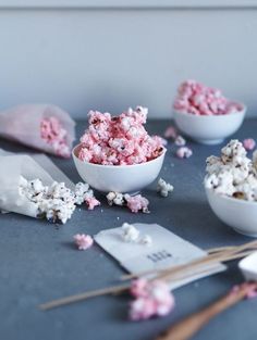 a bowl filled with pink and white popcorn next to other bowls full of marshmallows