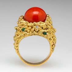 The textured ring is centered with a round, coral cabochon, glued in place. The coral is accented with seven (7) bead set, round mixed cut emeralds and six (6) bead set, round brilliant cut diamonds. The ring measures 21.6mm at the top, rises 15.7mm above the finger, tapering to 5.0mm wide and 1.1mm thick at the base of the shank. We offer complimentary ring sizing to fit. Formal Coral Jewelry With Cabochon Details, Formal Coral Jewelry With Cabochon, Luxury Round Coral Jewelry, Luxury Coral Jewelry For Formal Occasions, Elegant Coral Ring Jewelry, Formal Coral Ring, Luxury Red Coral Jewelry For Formal Occasions, Luxury Red Coral Jewelry, The Coral