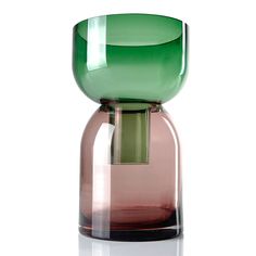 a green and pink glass vase sitting on top of a table next to a white wall