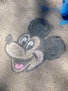 a mickey mouse drawn in the sand with a blue trash can nearby