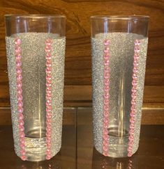 two glasses with pink beads on them sitting on a table next to a wooden wall