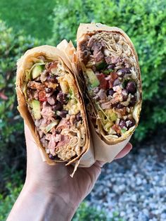 a hand holding a burrito filled with meat and veggies