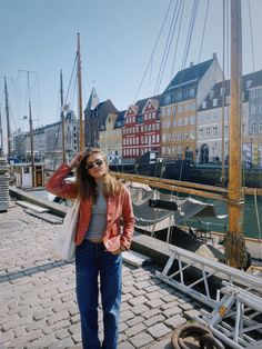 a woman standing on a dock next to some buildings and boats in the water with her hands behind her head