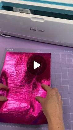 someone is cutting out pink foil on a piece of paper with a machine in the background