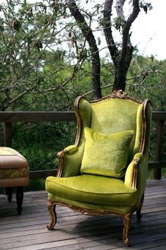 a green chair sitting on top of a wooden deck next to a tree with no leaves