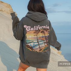 "Our Vintage California Sunset Hoodie - Embrace the essence of California with our cozy and luxurious hoodie featuring a striking retro design on the back.  With \"California\" in bold, distressed text overlaid on a mesmerizing art deco-style beach scene, complete with crashing waves, windblown trees, and a radiant sunset, this hoodie exudes West Coast vibes!  Crafted for ultimate comfort and warmth, it feels like an old favorite from the very first wear, making it a must-have for those who adore California's laid-back atmosphere. Whether you're a local or simply enamored with the Golden State, this hoodie serves as a cherished memento or a thoughtful gift for any occasion. .: 80% Ringspun US cotton, 20% Polyester .: Heavy fabric (9.5 oz /yd²) .: Relaxed fit - Please reference the size cha Oversized Long Sleeve Vsco Hoodie, Oversized Graphic Print Hoodie For Outdoor, Oversized Hoodie With Graphic Print For Outdoor, Oversized Cozy Hoodie With Graphic Print, Oversized Vsco Sweatshirt For Streetwear, Vsco Style Winter Hoodie For Streetwear, Vsco Style Long Sleeve Sweatshirt For Streetwear, Vsco Winter Hoodie For Streetwear, Oversized Vsco Style Hoodie