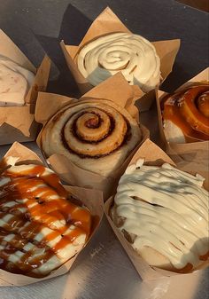 several different types of pastries on display in brown paper wrappers with white frosting and caramel swirls