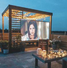 an outdoor movie screen is lit up at night with candles and lights on the ground