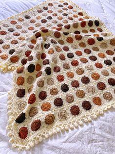 a crocheted blanket on top of a bed with white sheets and brown polka dots