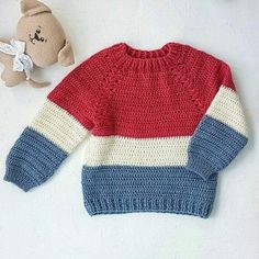 a red, white and blue sweater next to a teddy bear