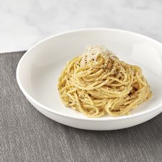 a white bowl filled with pasta on top of a gray place mat next to a knife and fork