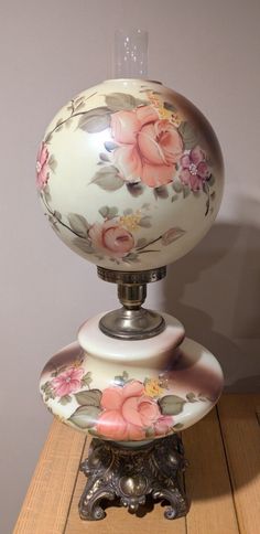 an old fashioned lamp with flowers painted on it's glass globe shader, sitting on top of a wooden table