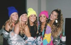 four beautiful young women standing next to each other in front of a tv screen wearing beanies