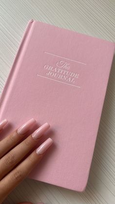 a woman's hand holding onto a pink book