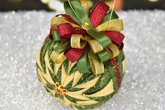 a christmas ornament with gold and red ribbons on it's side sitting on a silver surface