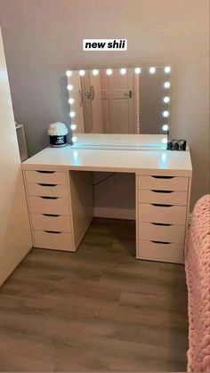 a white vanity with lights on it and a pink bed in front of the mirror