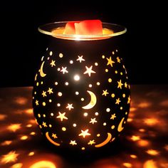 a lit candle holder with stars and moon designs on the lid, sitting on a table