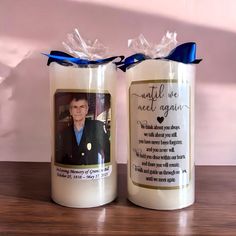 two personalized candles are sitting on a table with a blue ribbon around the top