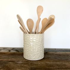 wooden spoons and utensils in a white ceramic cup on a wood table