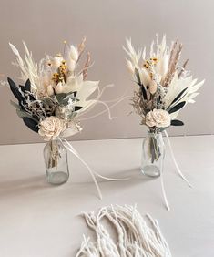 two vases with flowers are sitting on a table next to a white string and rope