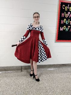 a woman in a red dress and checkered coat stands next to a chalkboard