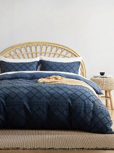 a bed with blue comforter and pillows in a room next to a wicker table